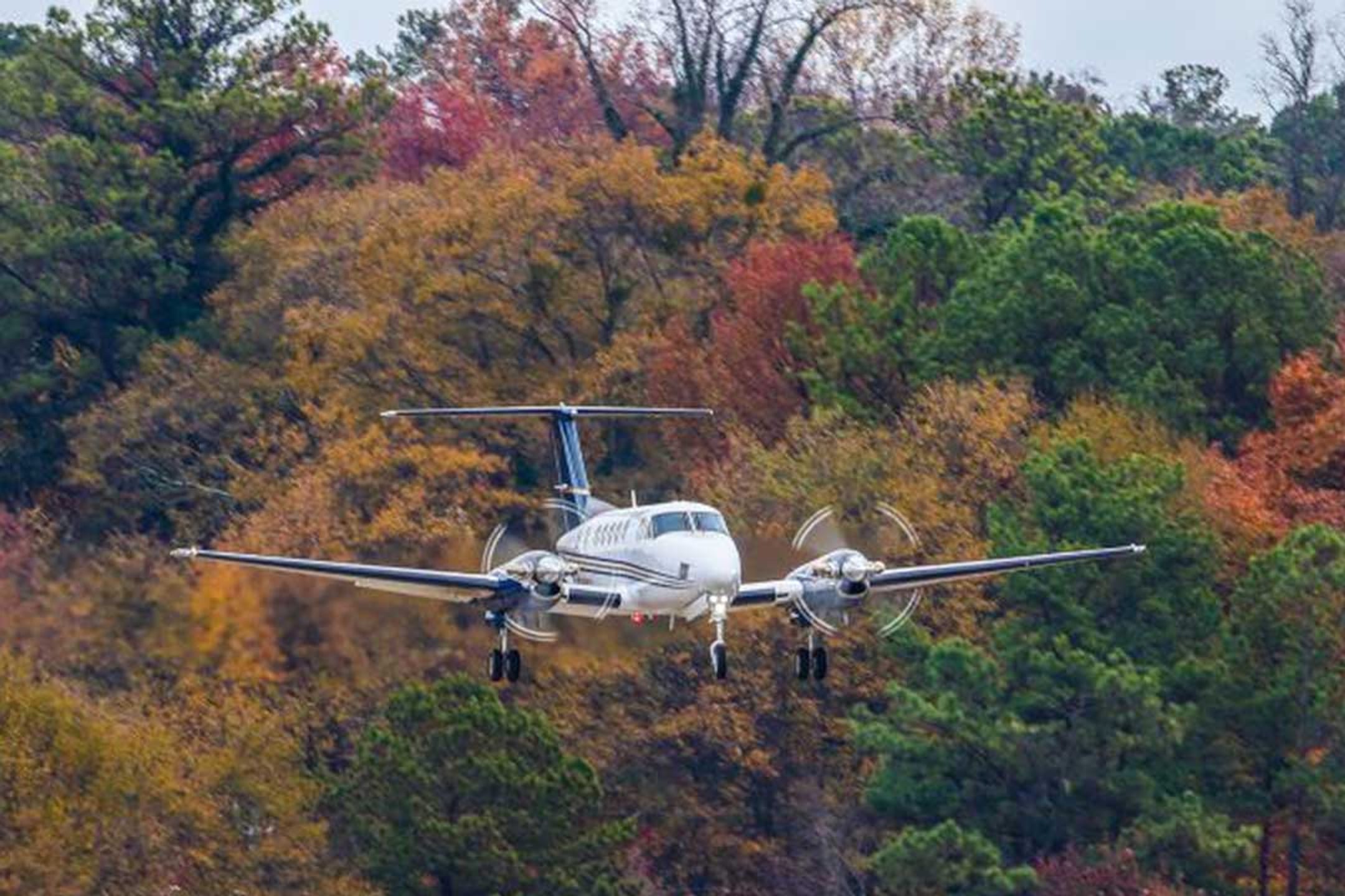 A King Air 350 on short final over autumn woodland