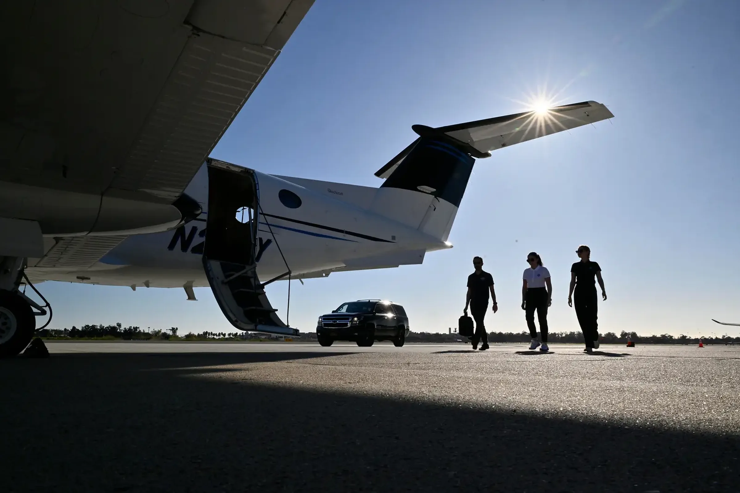 Clients walking from their car to a waiting King Air 350, airstair down, into the sun